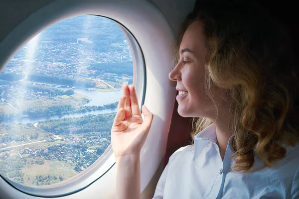 young woman in the cabin of a landing plane looks through the porthole at the terrain below