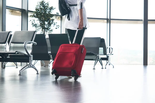 woman traveler with luggage climbs the stairs in airport or train station lounge; legs and suitcase close-up