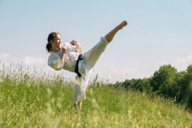 Genç kız dışarıda karate yapıyor, mawashi geri kick yapıyor.