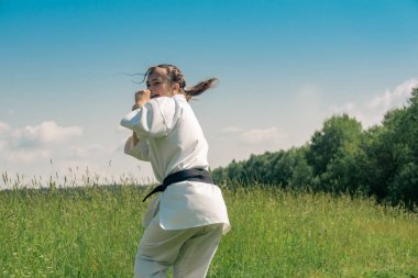 teenage girl practicing karate kata outdoors, prepares to uro mawashi geri (hook kick)