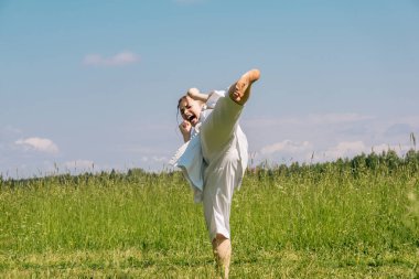 teenage girl practicing karate kata outdoors, performs the yoko geri kick with kiai