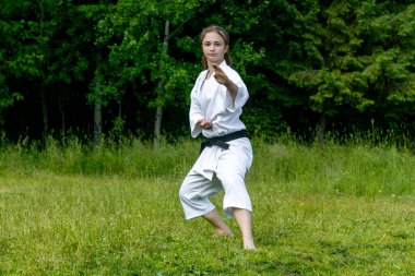 teenage girl practicing karate kata outdoors, performs soto uke or outside block in kakutsu dachi stand