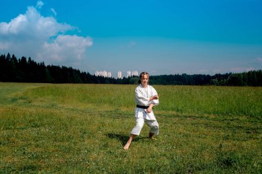 teenage girl practicing karate kata outdoors, prepares to perform downward block gedan barai in zenkutsu dachi stance