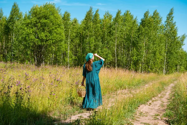 身穿民间农民服装 提着柳条筐的年轻女子沿着田野小路散步 — 图库照片