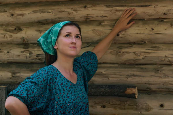 穿着传统农民服装和头巾的妇女梦游般地看着天空 背后是一堵木头墙 — 图库照片