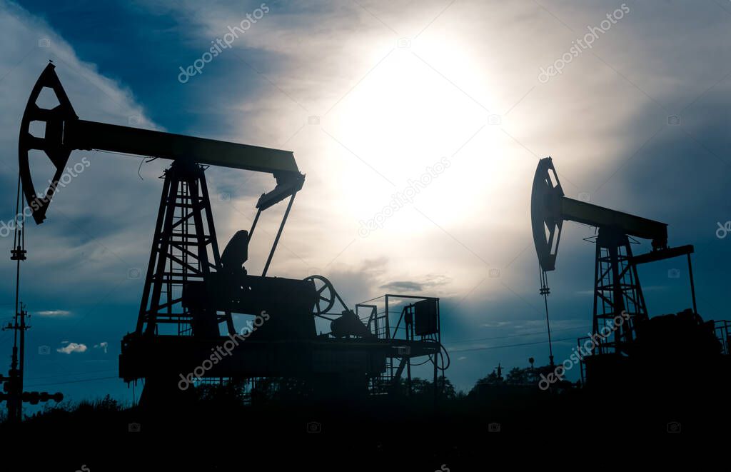 silhouettes of pumpjacks with piston pump on an oil wells against the background of an alarming sky