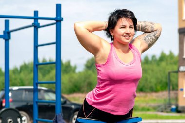 Genç bir kadın dış mekan egzersiz makinesi hiper uzantı benc kullanarak gerileme egzersizleri yapıyor.