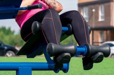 Genç bir kadın karın egzersizleri yapıyor. Açık hava egzersiz makinesi oturma tezgahı kullanıyor.