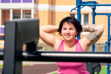 Şehir avlusunda arka ek egzersizler yapan genç bir kadın sokak egzersiz makinesi hiper uzantısını kullanıyor.