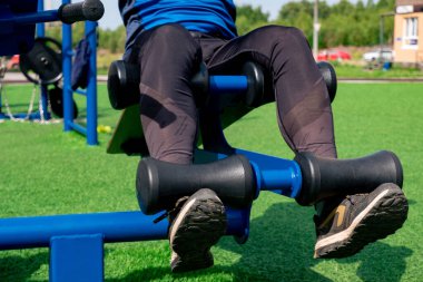 Bir insanın bacakları, karın egzersizleri yapıyor. Açık hava egzersiz makinesi oturma tezgahı kullanıyor.