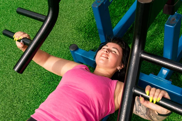 Genç bir kadın şehir avlusunda ağırlık kaldırma makinesi kullanarak egzersiz yapıyor.