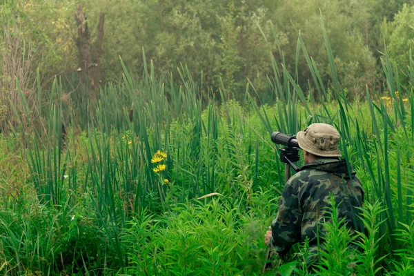 man birdwatcher makes field observation with a spotting scope standing among the tall grass