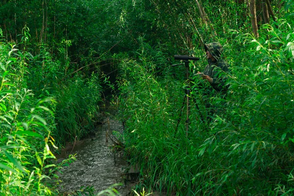 man birdwatcher makes observations in the wild with a spotting scope among the thickets in a river valley