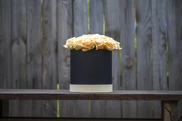 Creamy roses bouquet in black gift box on the background of wooden fence.