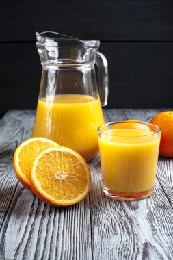 Bardak taze portakal suyu, sürahi ve yarım portakal ahşap tablo