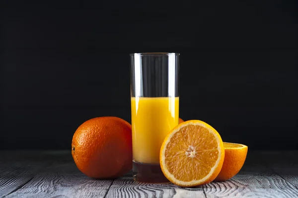 Szklanka świeżego soku pomarańczowego i pomarańcze na drewnianym stole. — Zdjęcie stockowe