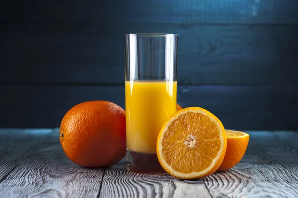 Szklanka świeżego soku pomarańczowego i pomarańcze na drewnianym stole. — Zdjęcie stockowe