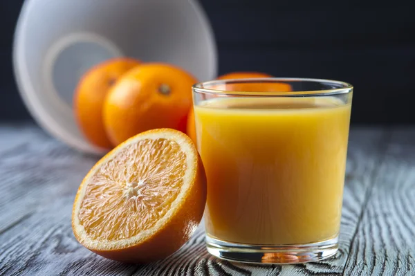 Sumo de laranja fresco e laranjas na mesa de madeira . — Fotografia de Stock