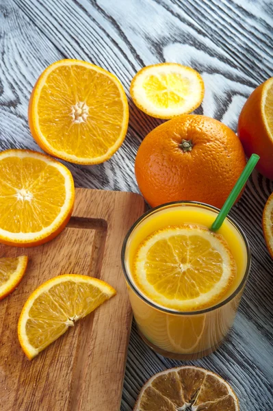 Copo de suco de laranja fresco e laranjas na mesa de madeira . — Fotografia de Stock