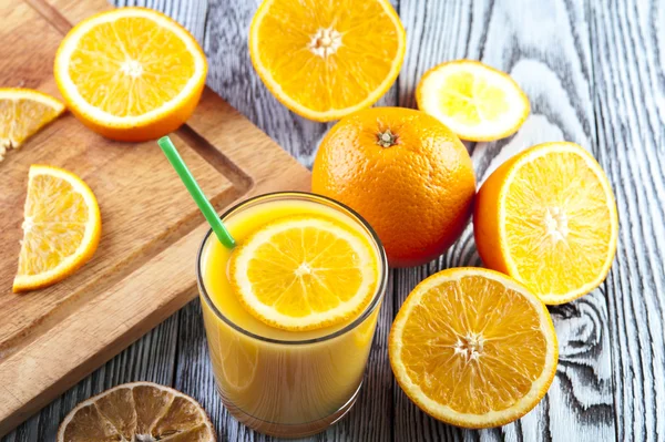 Copo de suco de laranja fresco e fatias de laranja na mesa de madeira . — Fotografia de Stock