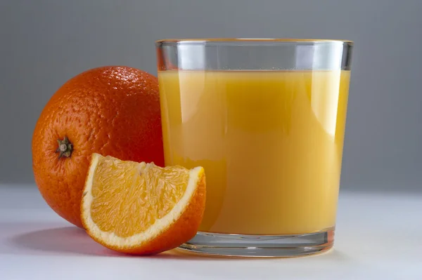 Pohár frissen facsart narancslével és a narancs a táblázat. — Stock Fotó