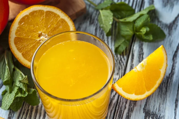 Vaso de zumo de naranja, hojas de menta y naranjas sobre mesa de madera —  Fotos de Stock