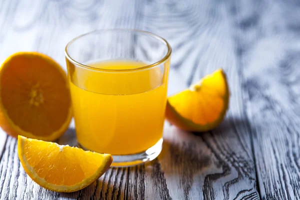 Świeży sok pomarańczowy z plastrami pomarańczy na drewnianym stole — Zdjęcie stockowe