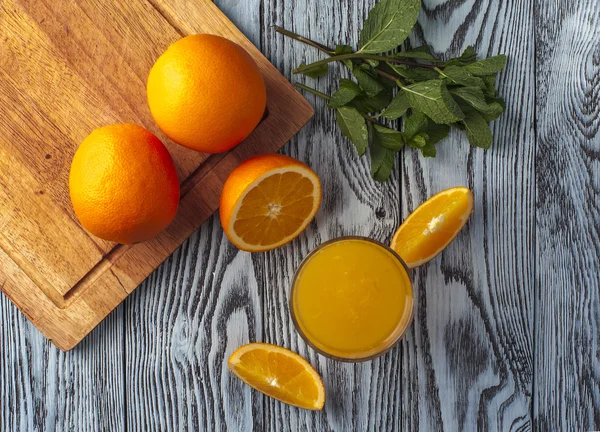 Copo de suco de laranja, folhas de hortelã e laranjas — Fotografia de Stock