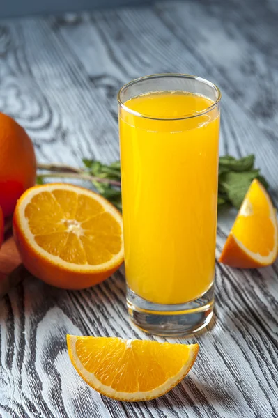 Świeży sok pomarańczowy, pomarańczowy plastry i liści mięty na drewnianym stole — Zdjęcie stockowe