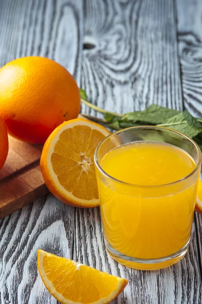 Copo de suco de laranja, folhas de hortelã e laranjas na mesa de madeira — Fotografia de Stock