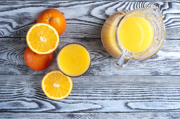 Sumo de laranja recentemente espremido, laranjas e jarro na mesa de madeira — Fotografia de Stock