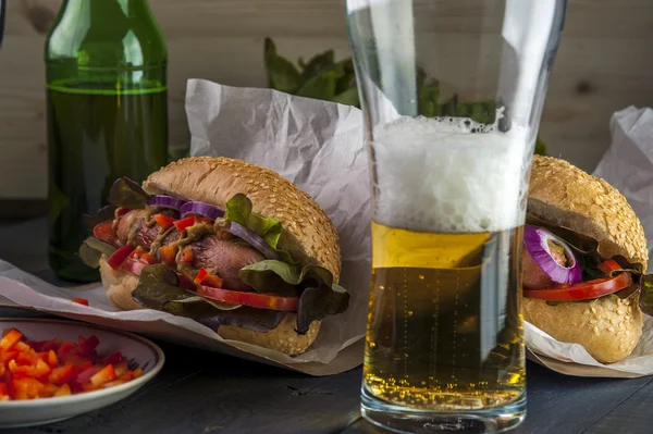Üveg sört és két hotdogs, sült kolbásszal és zöldség — Stock Fotó
