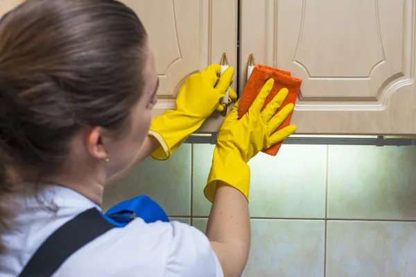 Mulher zeladora esfregando o armário da cozinha com um pano — Fotografia de Stock