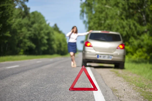 Triangle warning sign on the road and woman with her car after b — Stock Photo, Image