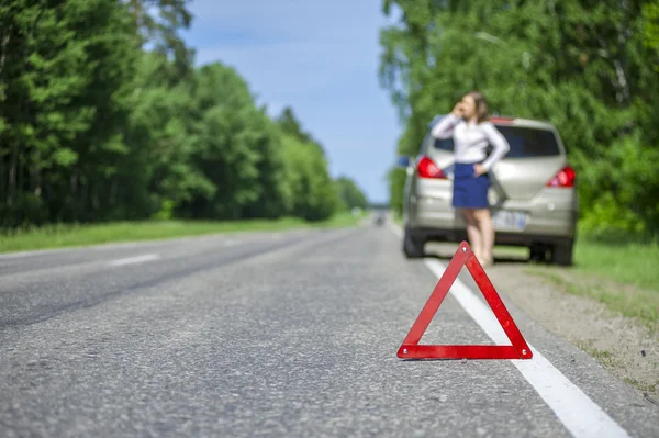 Red triangle sign on the road and Young woman calling for car as — Stock Photo, Image