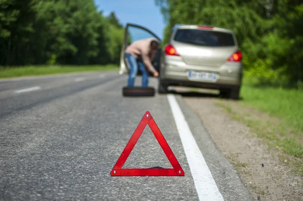 Kırık araba, acil durum işareti ve stepne adamla.