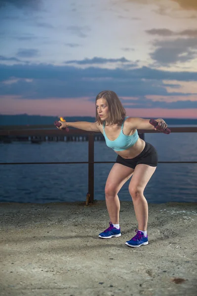 Young woman doing exercise with dumbbells on sea pier — Stock Photo, Image