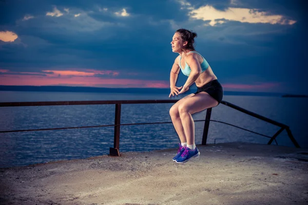 Young woman doing squat jumps on pier