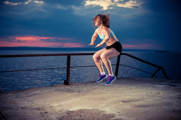 Fit woman in sportswear doing squat jumps