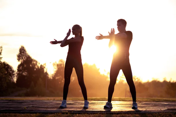 Silhouettes of young adults exercising at sunset — Stock Photo, Image