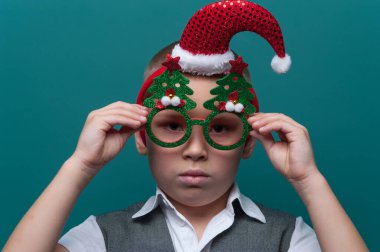 Noel Baba şapkalı küçük bir çocuğun portresi ve Noel ağaçlı komik gözlükler.