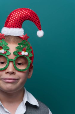 Noel Baba şapkalı küçük mutlu çocuk portresi ve Noel ağaçlı komik gözlükler.