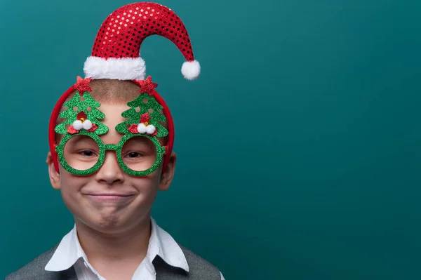 Ritratto di felice allegro ragazzo che indossa fascia con cappello di Babbo Natale e occhiali divertenti con alberi di Natale Foto Stock Royalty Free