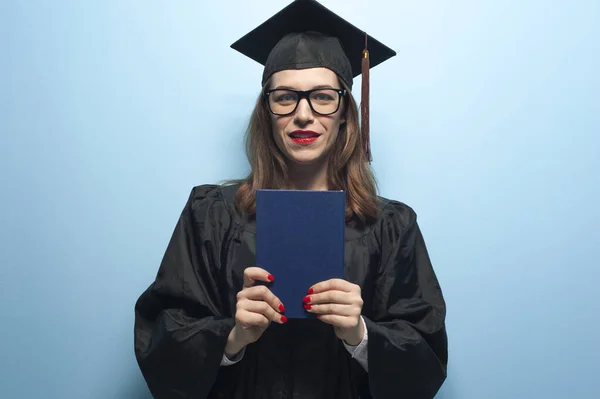 Urocza studentka nosząca czarny płaszcz i stojąca z dyplomem w rękach — Zdjęcie stockowe