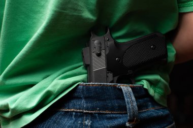 Küçük çocuk t-bok giyiyor ve kotlar sırtında silah taşıyor..