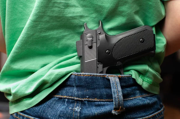 Anak kecil mengenakan t-shitr dan celana jeans memegang pistol di belakang punggungnya. Stok Gambar