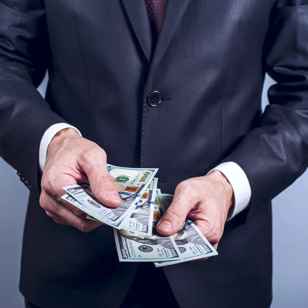 Man in een pak houdt ons dollar op grijze achtergrond — Stockfoto