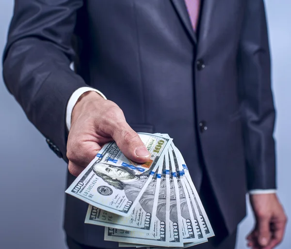 Man in a suit holds US dollars on grey background — Stock Photo, Image