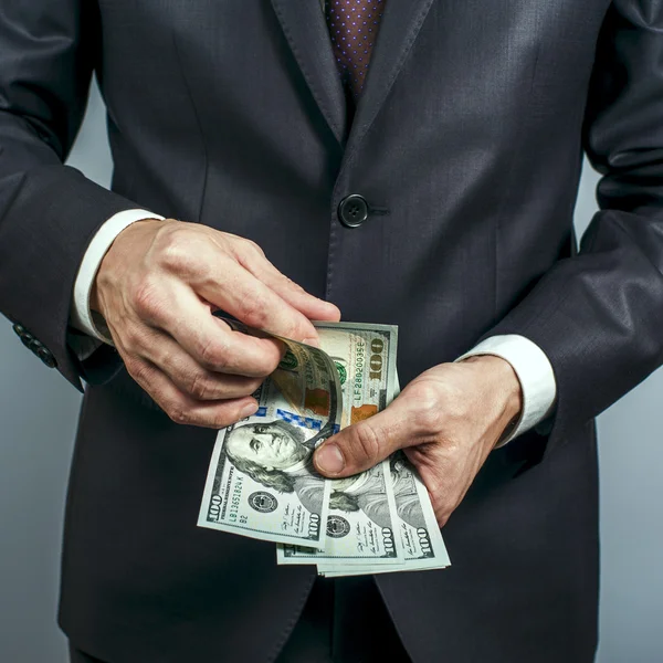 Człowiek w garniturze trzyma nas dolarów na szarym tle — Zdjęcie stockowe