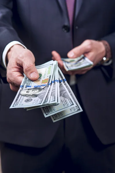 Homem de terno escuro dá a mão com dinheiro — Fotografia de Stock